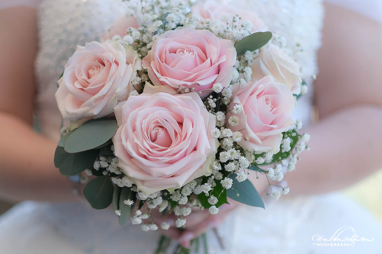 Bouquet de la mariée en gros plan, tenue par celle-ci de couleur rose pastel et blanc
