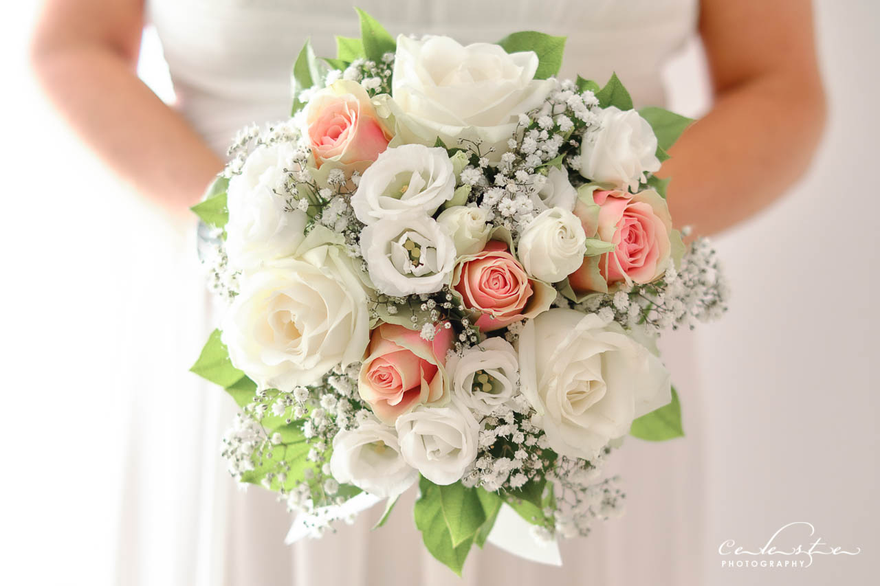Bouquet de la mariée rose pastel blanc et vert en gros plan tenue par la mariée sur fond blanc